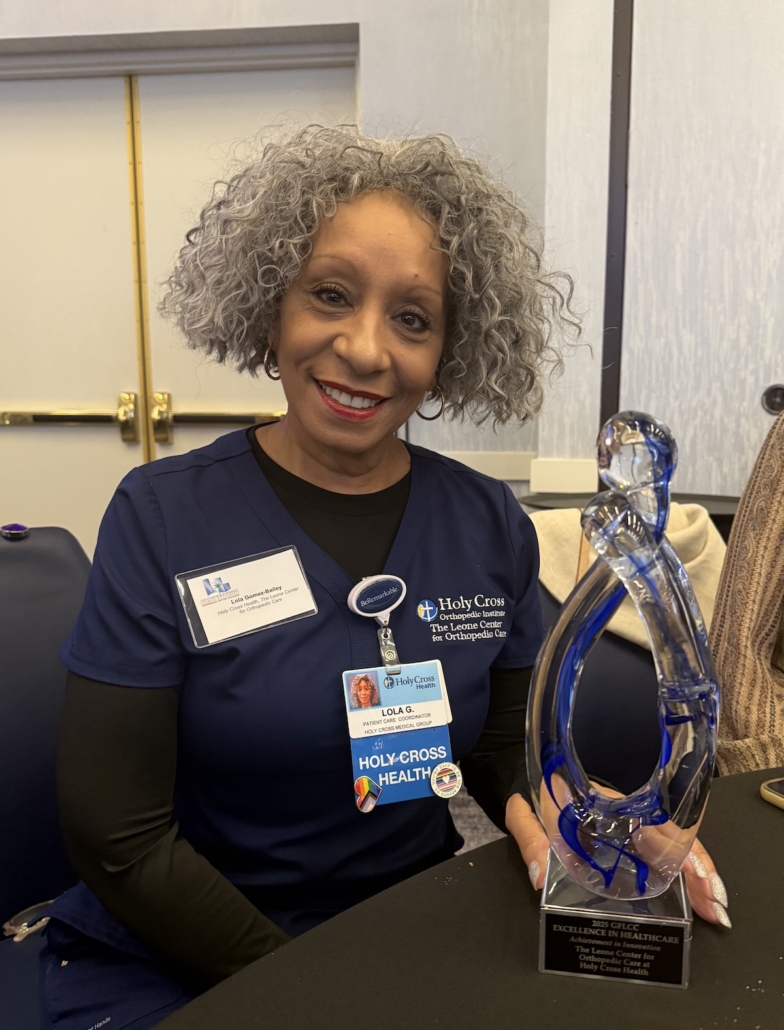 Secretary Lola at the Leone center for Orthopedic Care in front of Dr. Leone's excellence in healthcare award. 